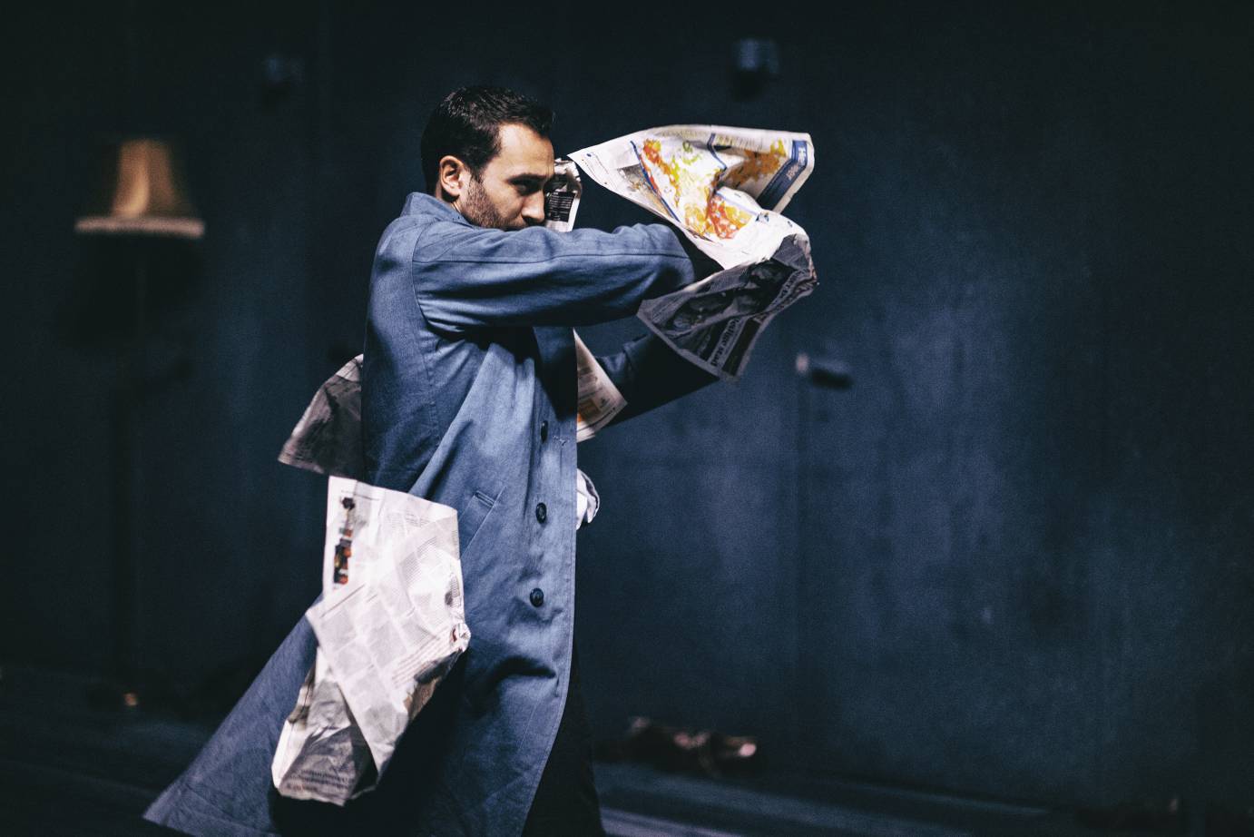 A newspaper wraps itself around a man in a denim jumpsuit 